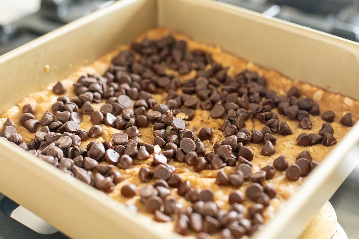 A layer of chocolate chips on a gold pan of cookie bars