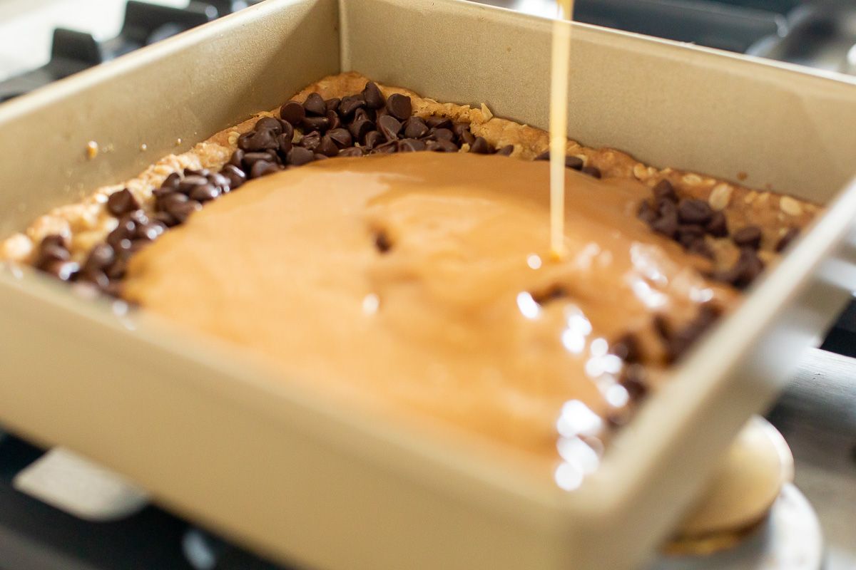 Melted caramel pouring over chocolate chips in a pan of cookie bars