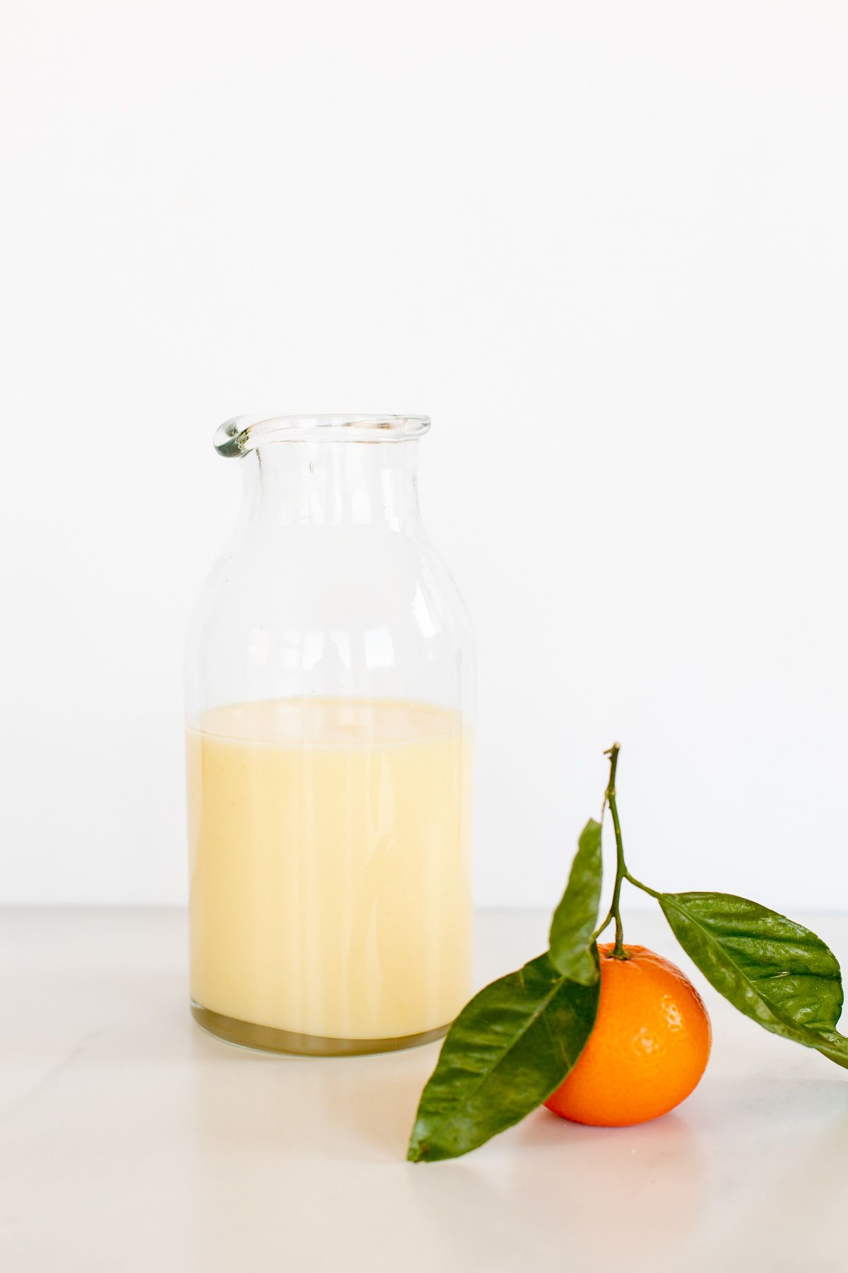 A clear glass jar of glaze with a single orange next to it. 
