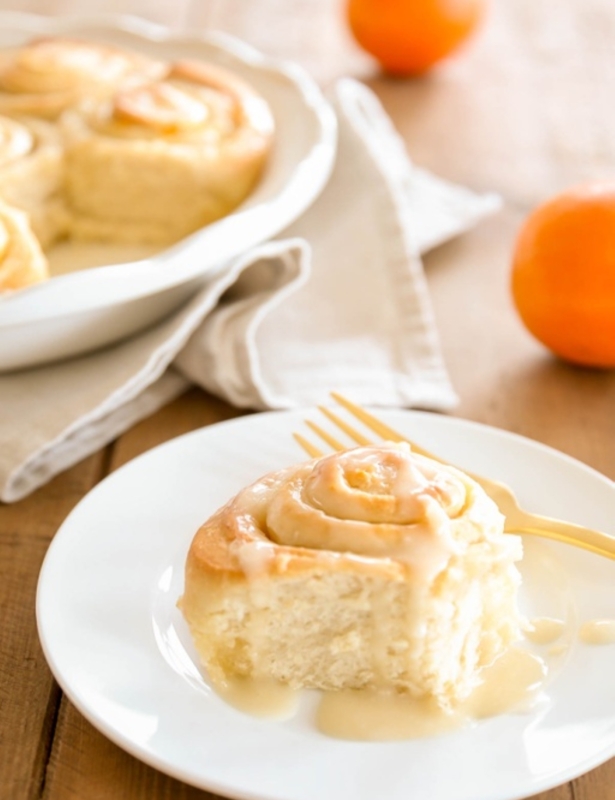An orange roll covered in orange glaze on a white plate.