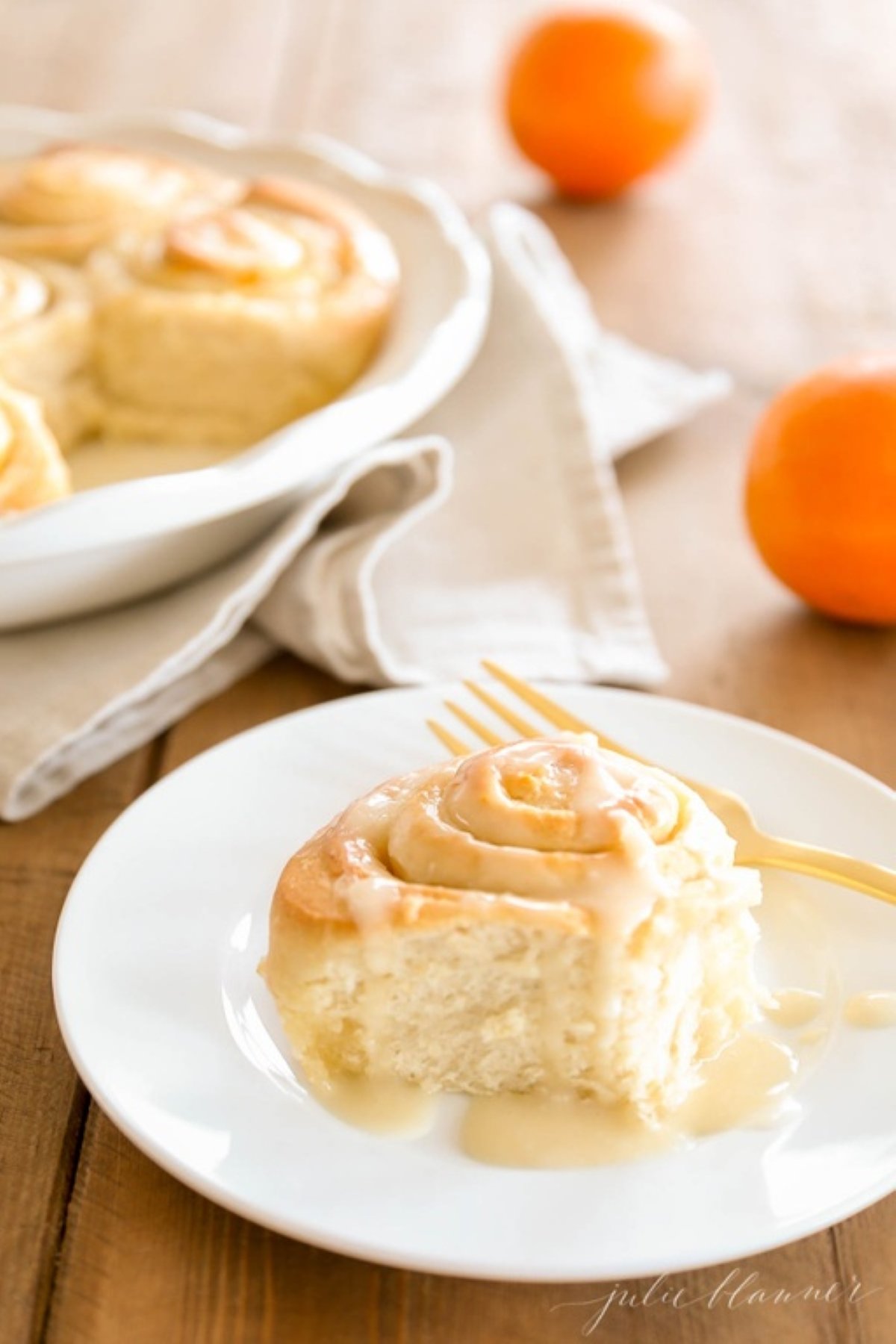 An orange roll covered in orange glaze on a white plate.