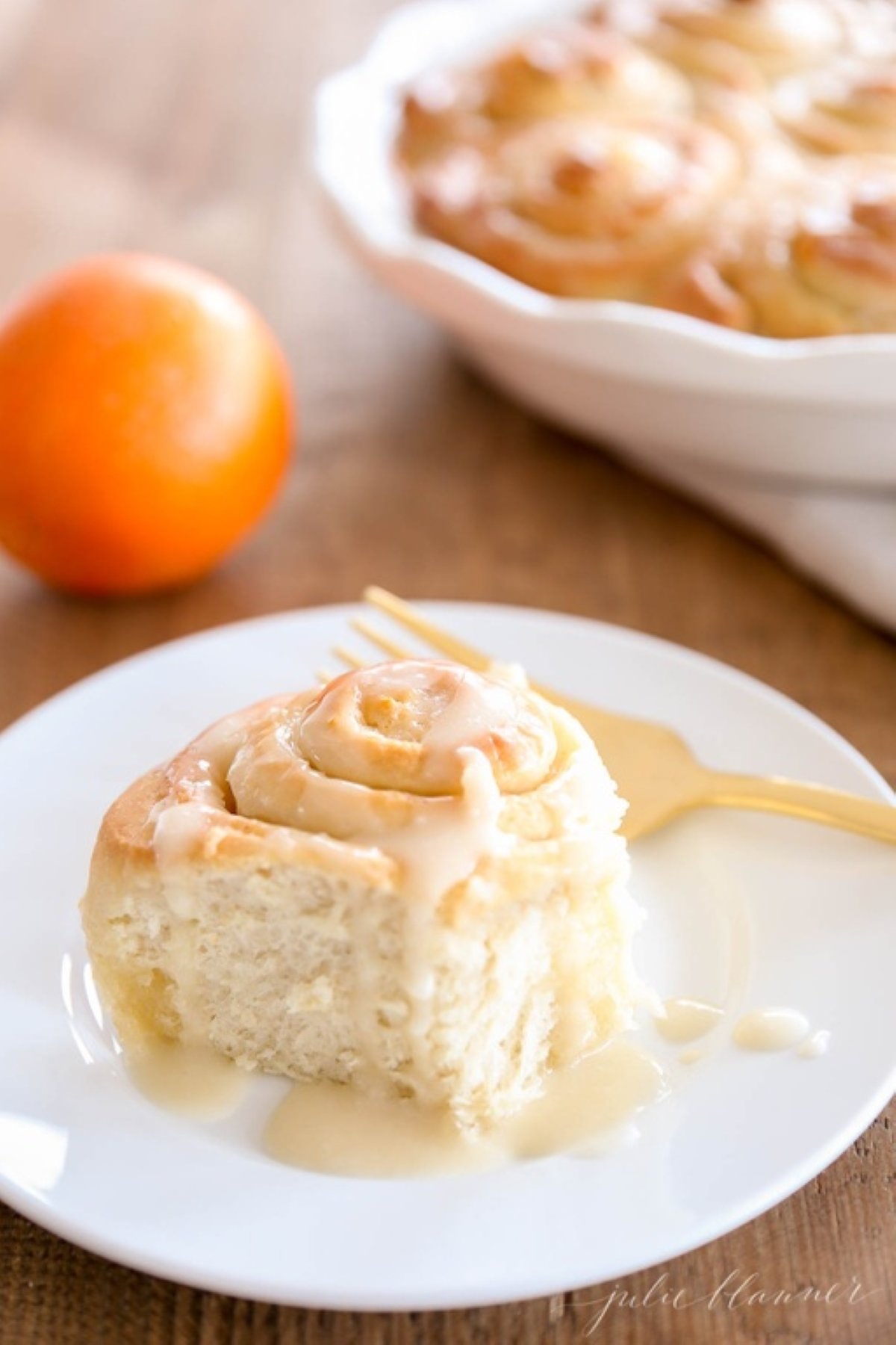 An orange roll covered in orange glaze on a white plate.