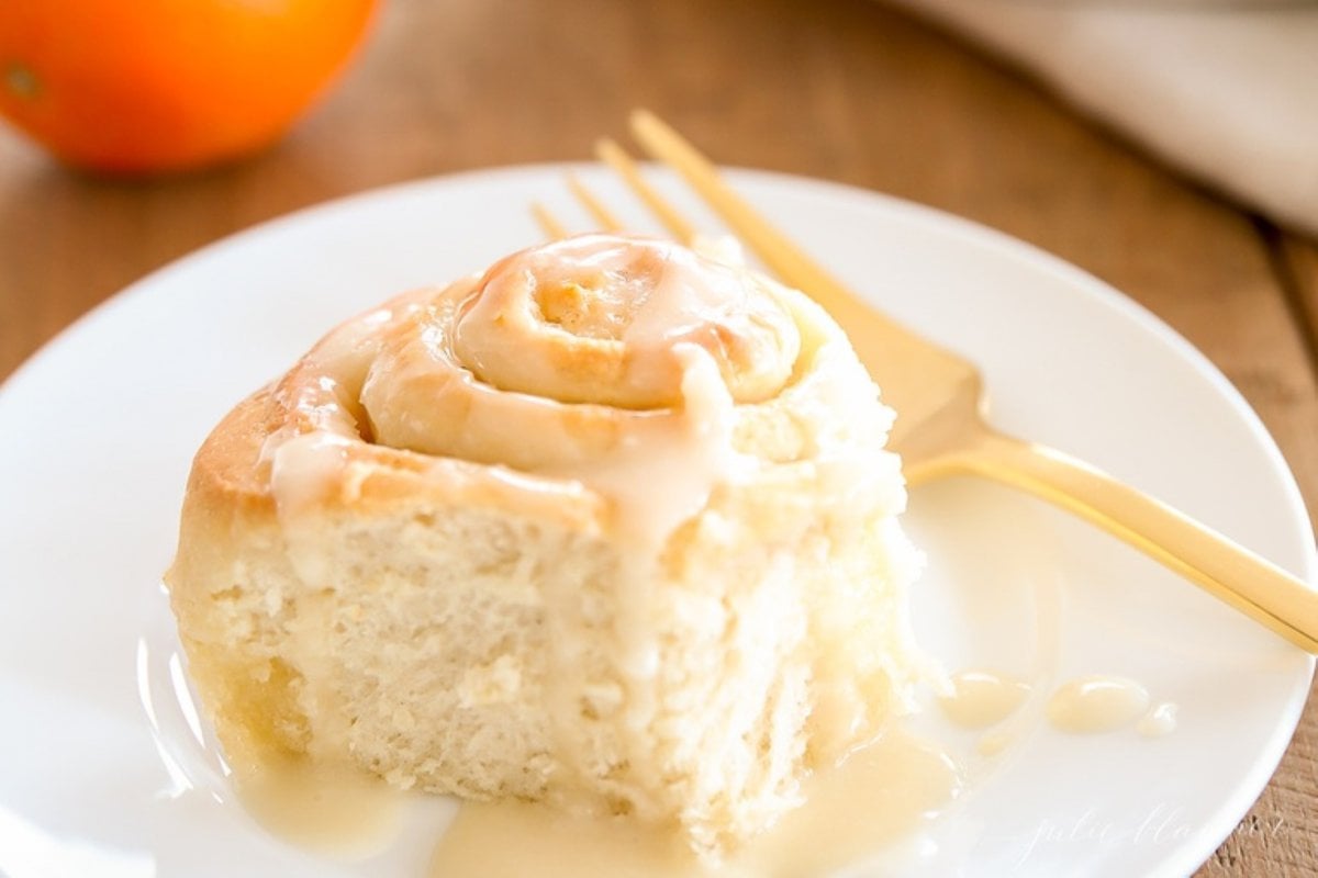 An orange roll covered in orange glaze on a white plate.