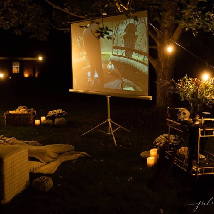 An outdoor movie set up in a yard for halloween, with a skeleton, candles and decorations.