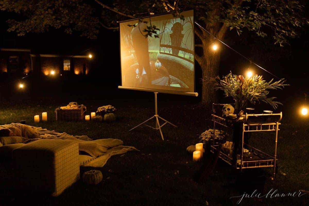 An outdoor movie set up in a yard for halloween, with a skeleton, candles and decorations.