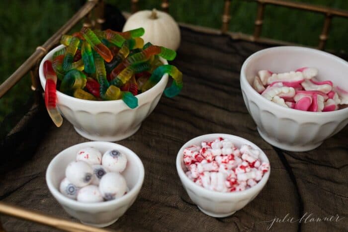 Halloween party snacks set up in white bowls on a gold bar cart.