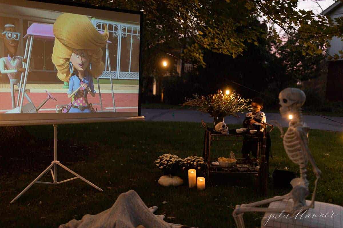 An outdoor movie set up in a yard for halloween, with a skeleton, candles and decorations.