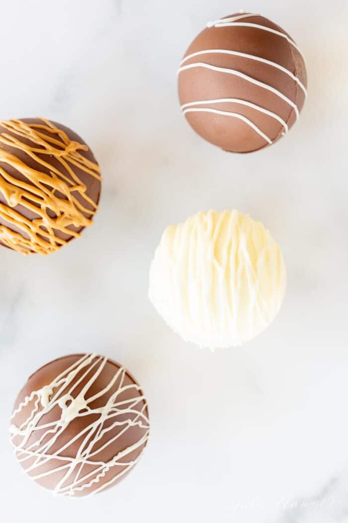 Peanut butter hot chocolate bombs on a marble surface, drizzled with peanut butter and white chocolate.