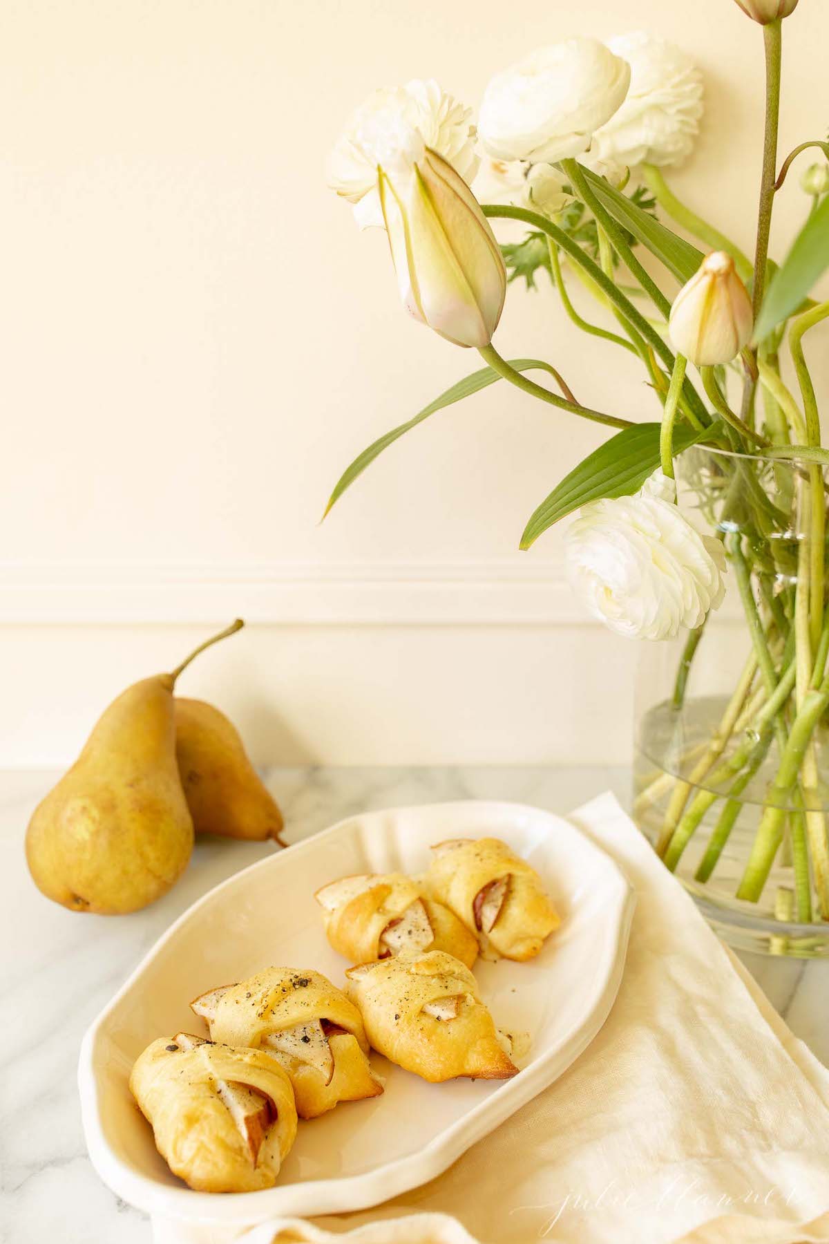 Pear crescent roll appetizers on a white platter. Fresh flowers and fall pears in the background. 
