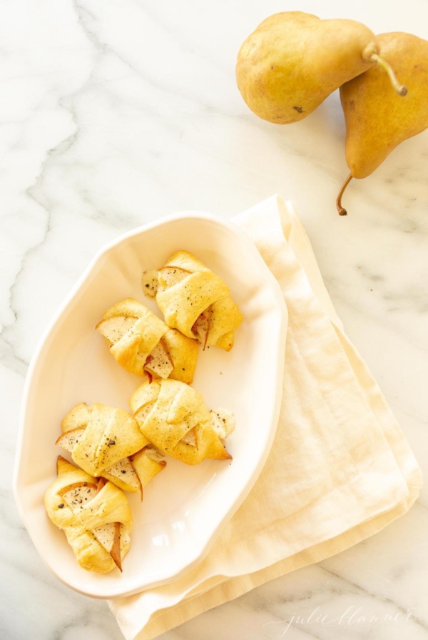 Pear crescent roll appetizers in a white basket lined with a pink linen towel.