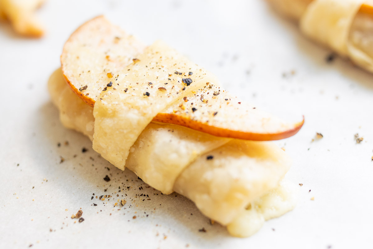 Pear wrapped crescent roll appetizers on a parchment lined baking sheet.