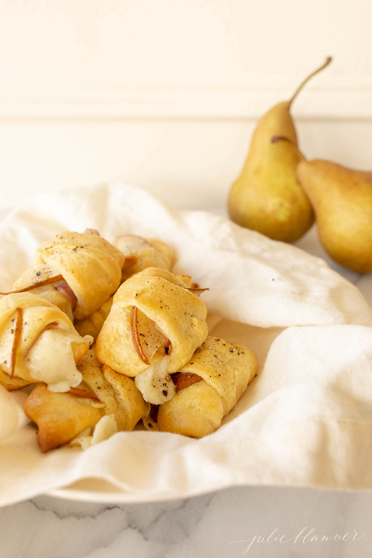 Pear crescent roll appetizers in a white basket lined with a pink linen towel.