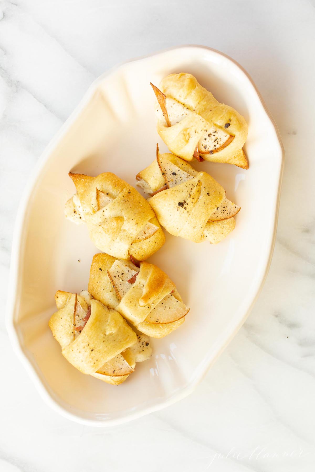 Pear crescent roll appetizers in a white basket lined with a pink linen towel.