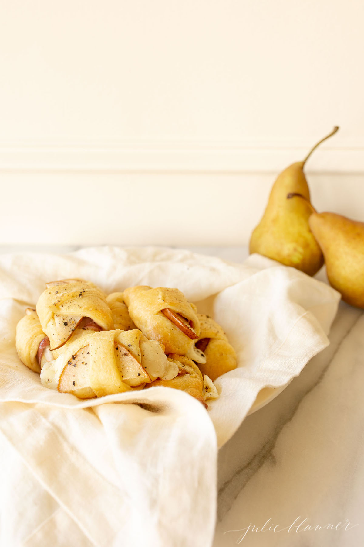 Pear crescent roll appetizers in a white basket lined with a pink linen towel.
