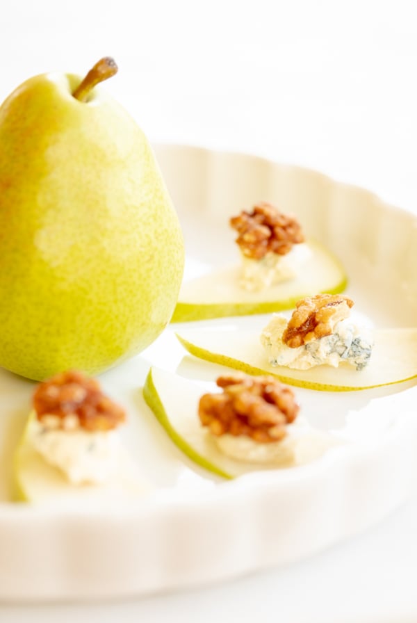 Walnut, blue cheese and sliced pear appetizers on a white platter.