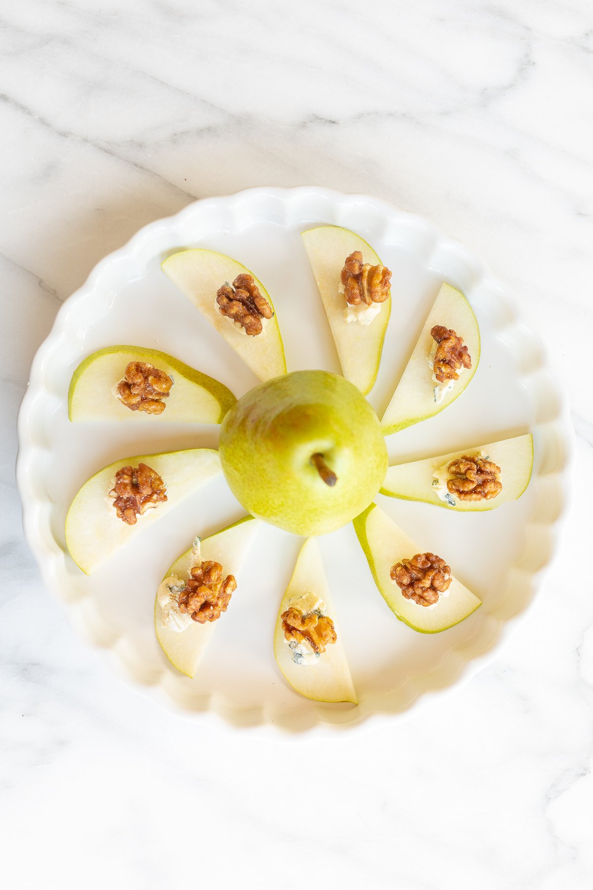 Walnut, blue cheese and sliced pear appetizers on a white platter.