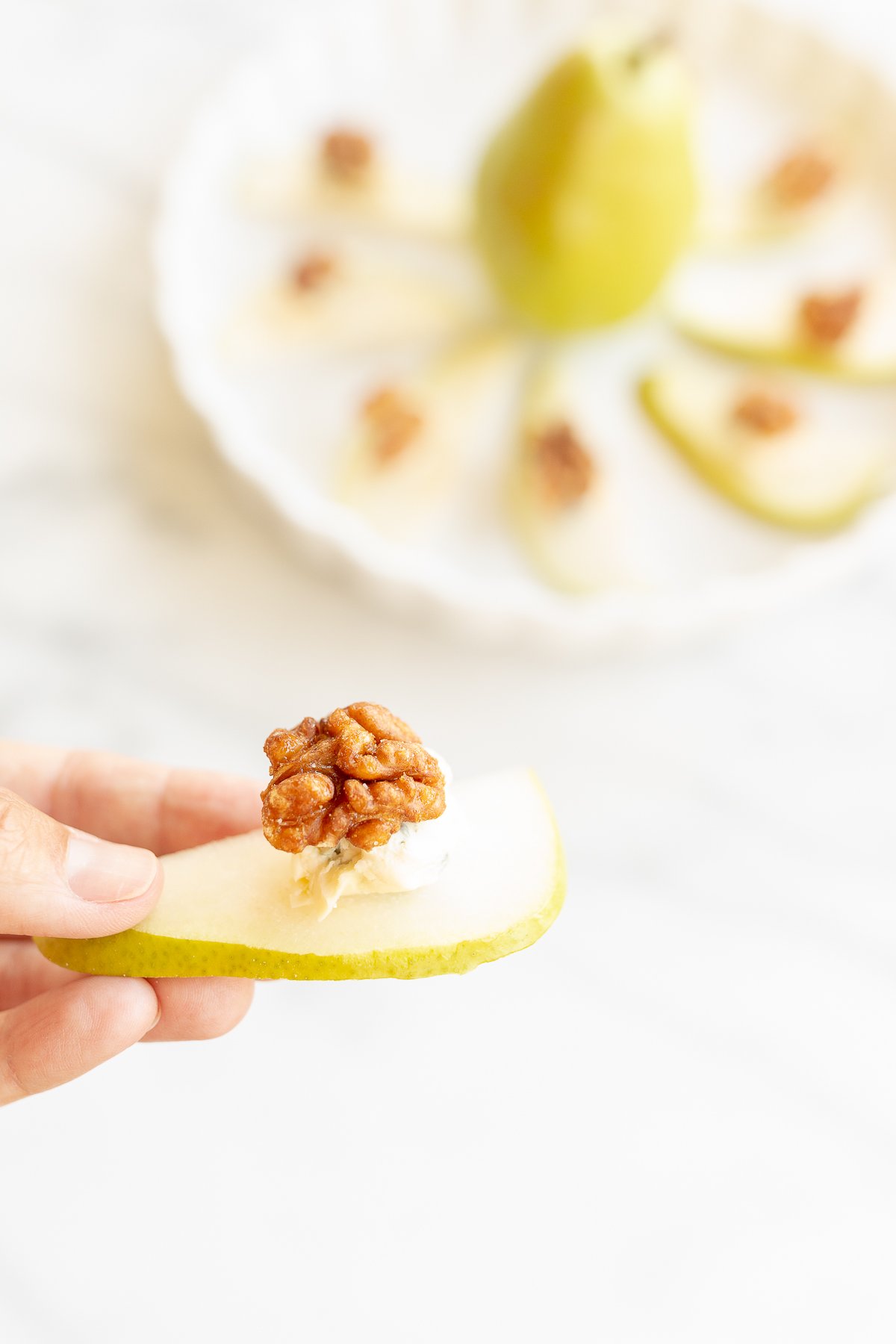 A hand holding a slice of pear topped with a walnut and blue cheese.