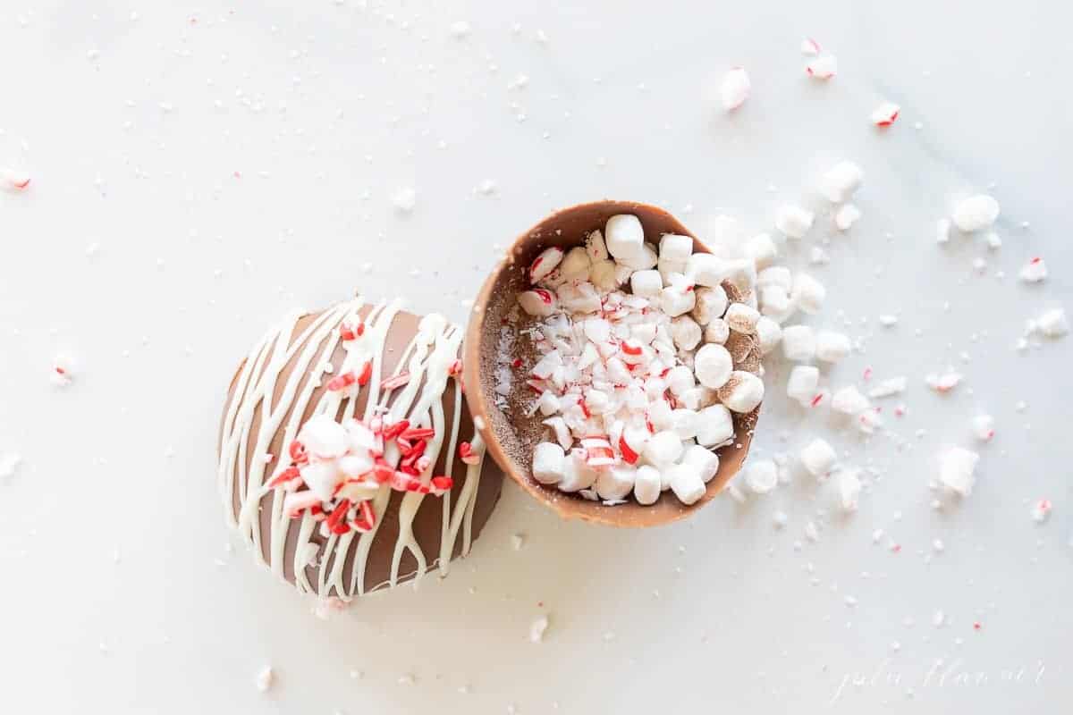A peppermint hot chocolate bomb, with marshmallows, cocoa mix and peppermint spilling out onto a marble surface.