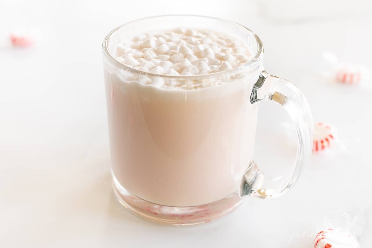 A clear glass mug of peppermint hot chocolate, topped with tiny marshmallows and crushed peppermint.