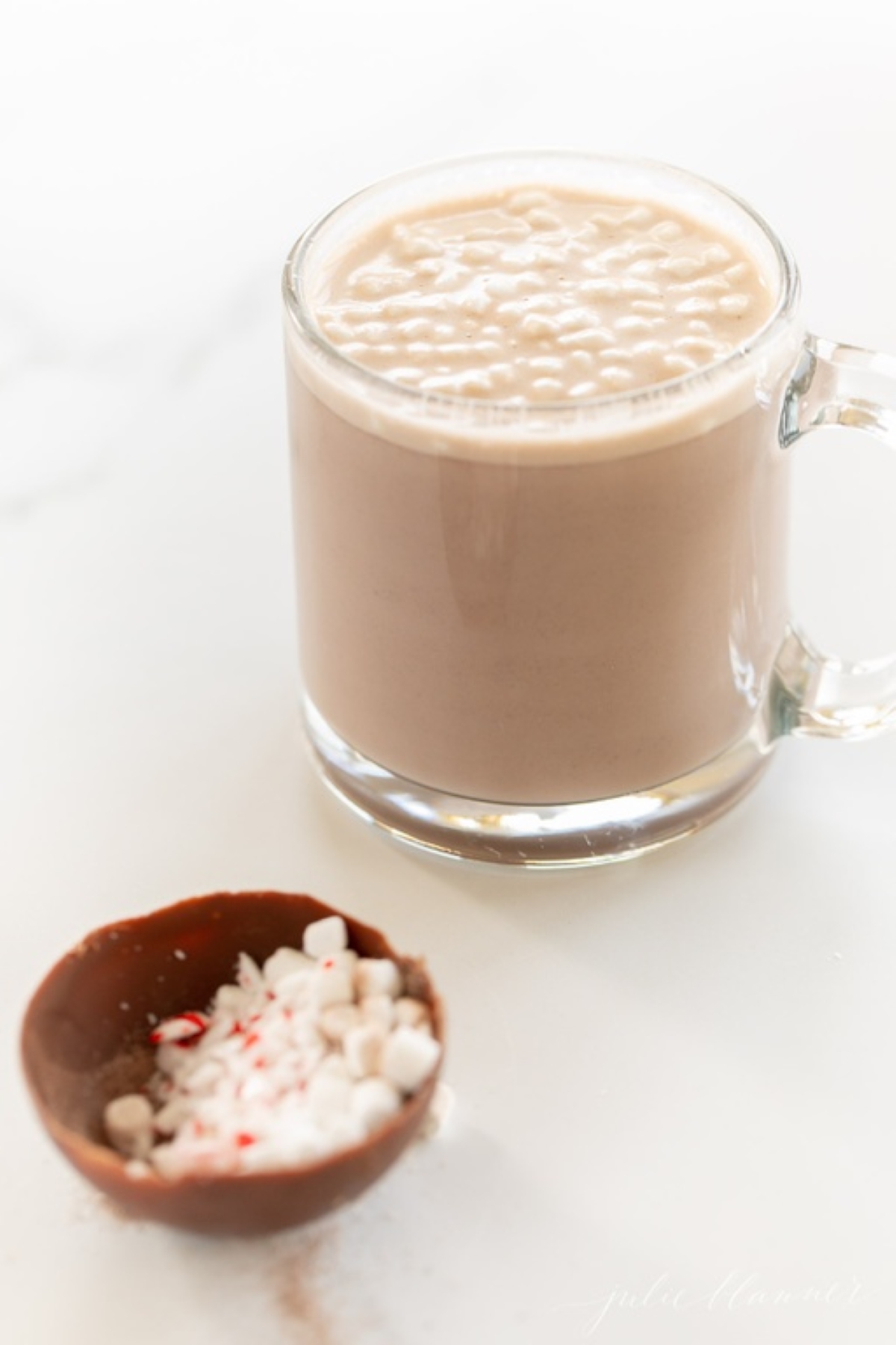 A mug of peppermint hot chocolate with half a hot chocolate bomb near.