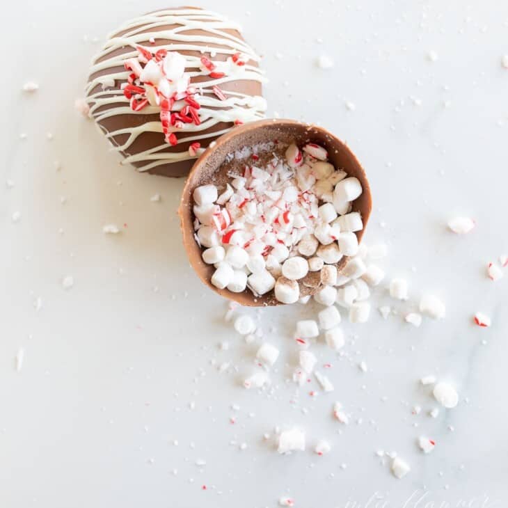 A peppermint hot chocolate bomb, with marshmallows, cocoa mix and peppermint spilling out onto a marble surface.