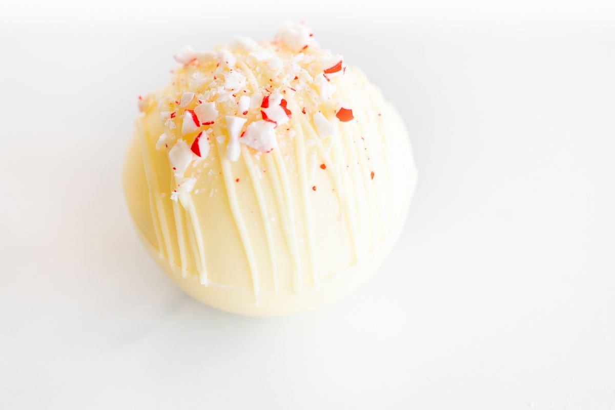 A white peppermint hot chocolate bomb on a white marble countertop