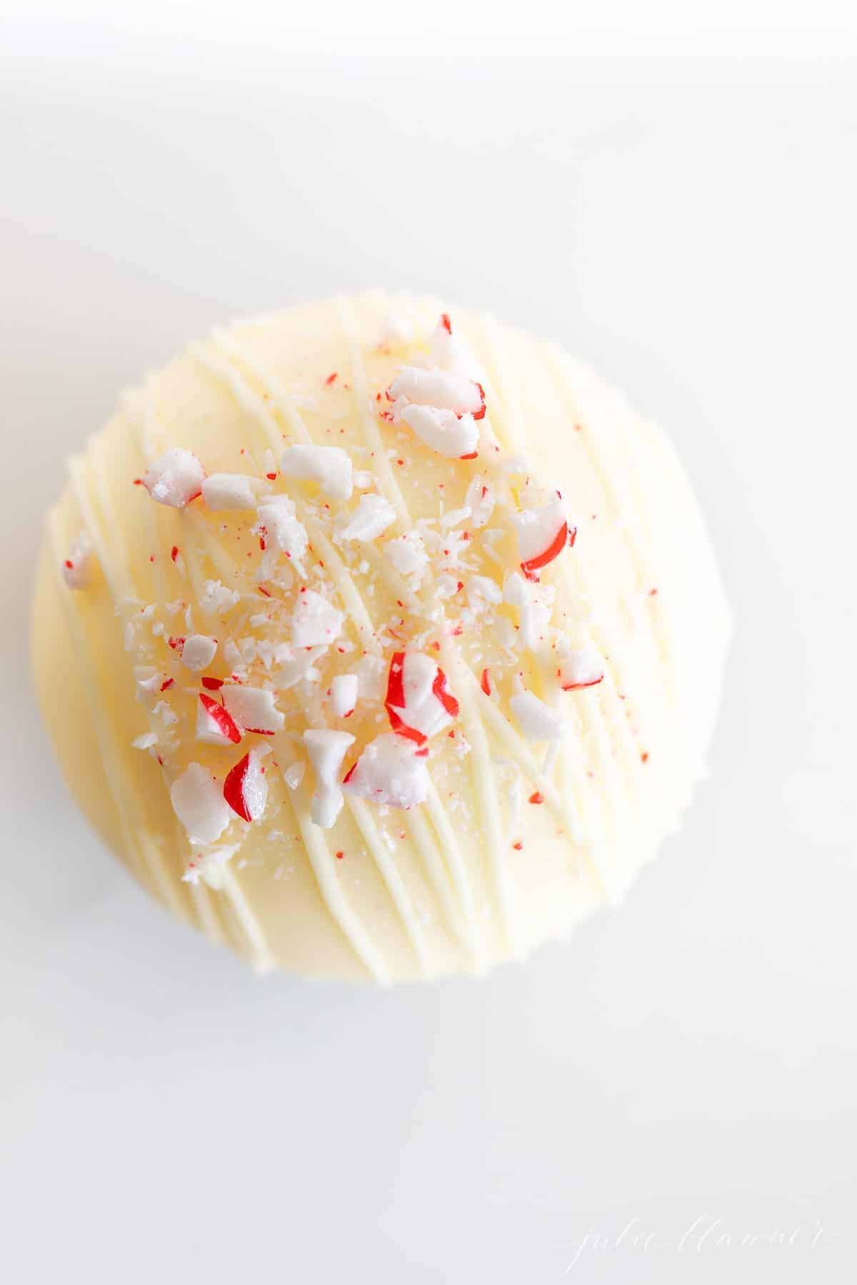 A white chocolate hot chocolate bomb topped with crushed peppermint on a marble surface.