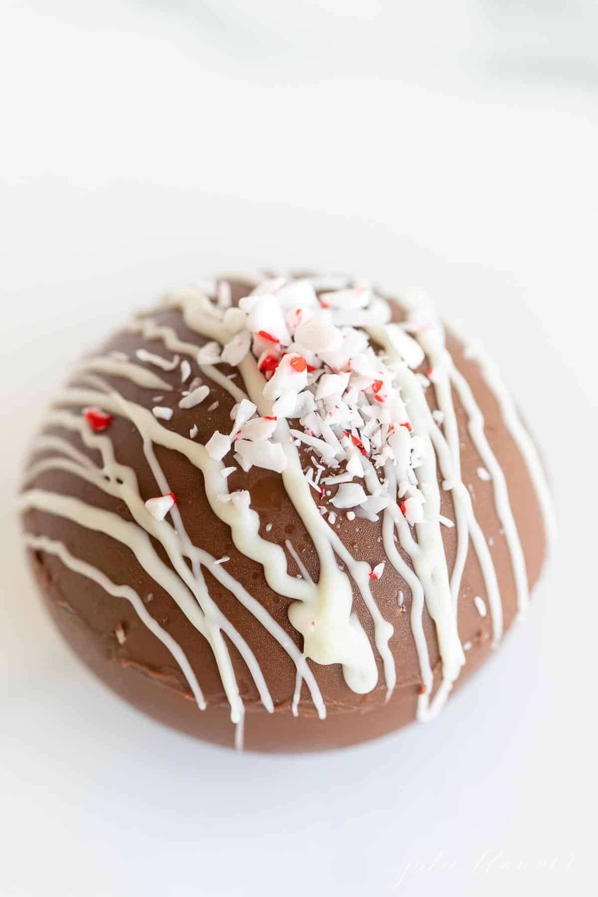 Hot chocolate bomb topped with crushed peppermint on a marble surface.