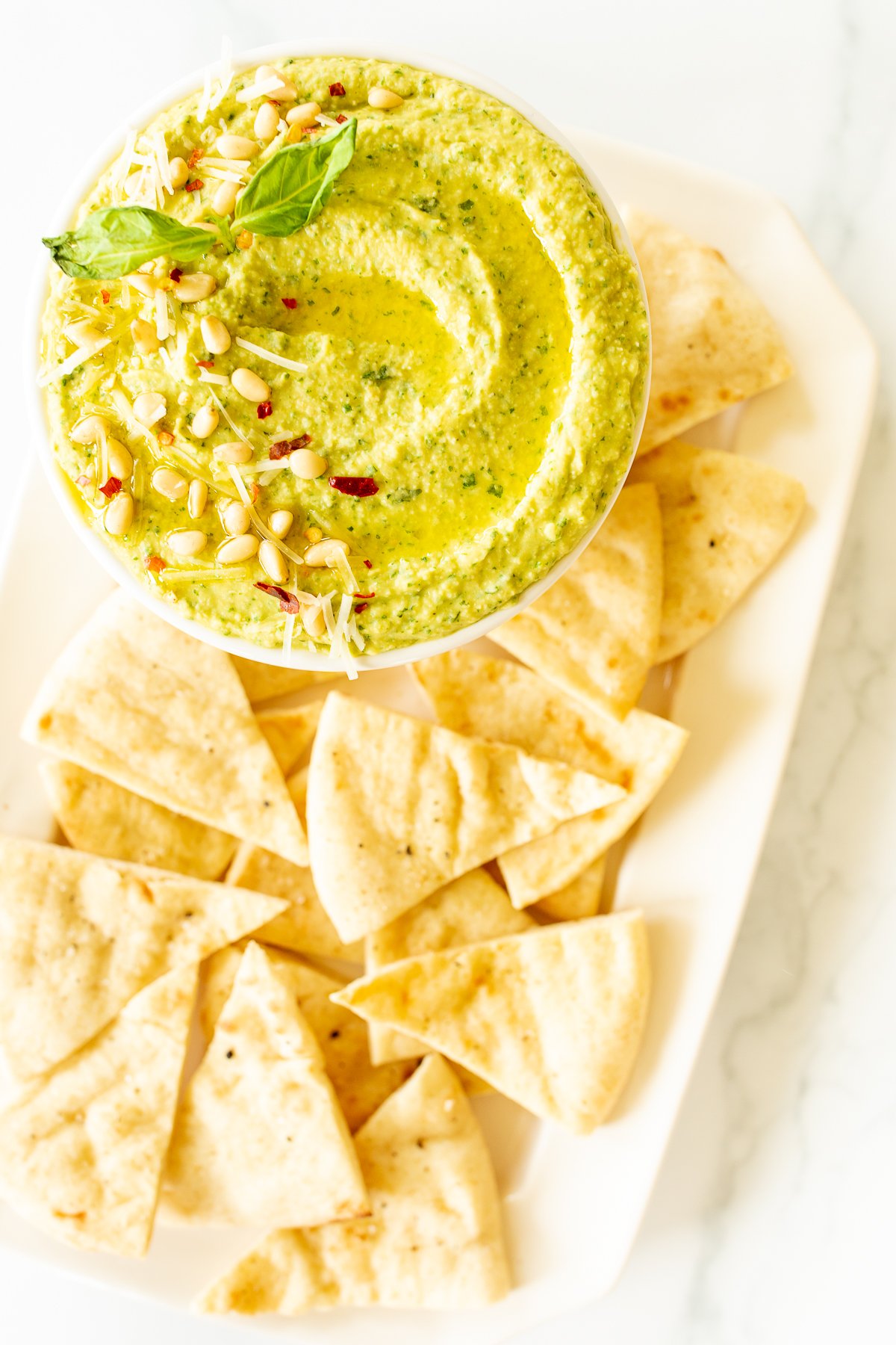 Pesto hummus in a white bowl surrounded by pita bread.