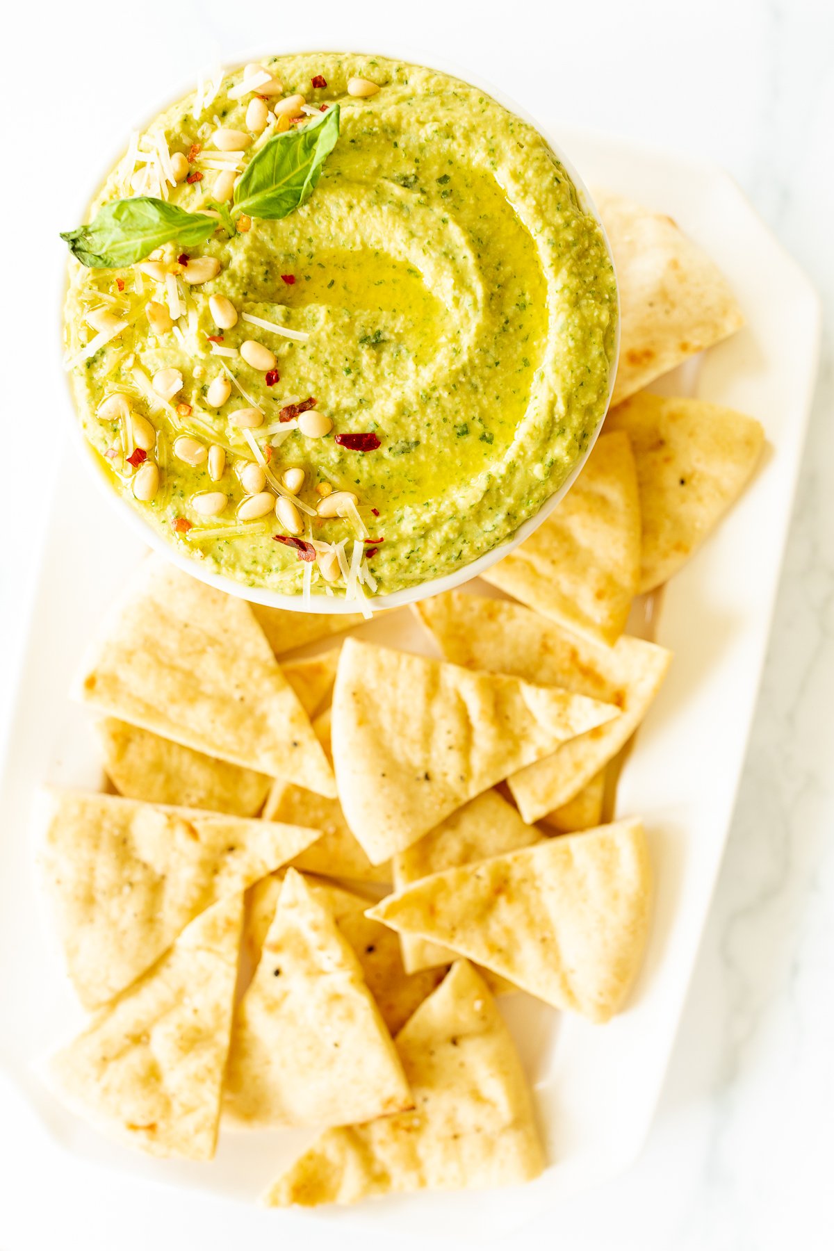 Pesto hummus in a white bowl surrounded by pita bread.