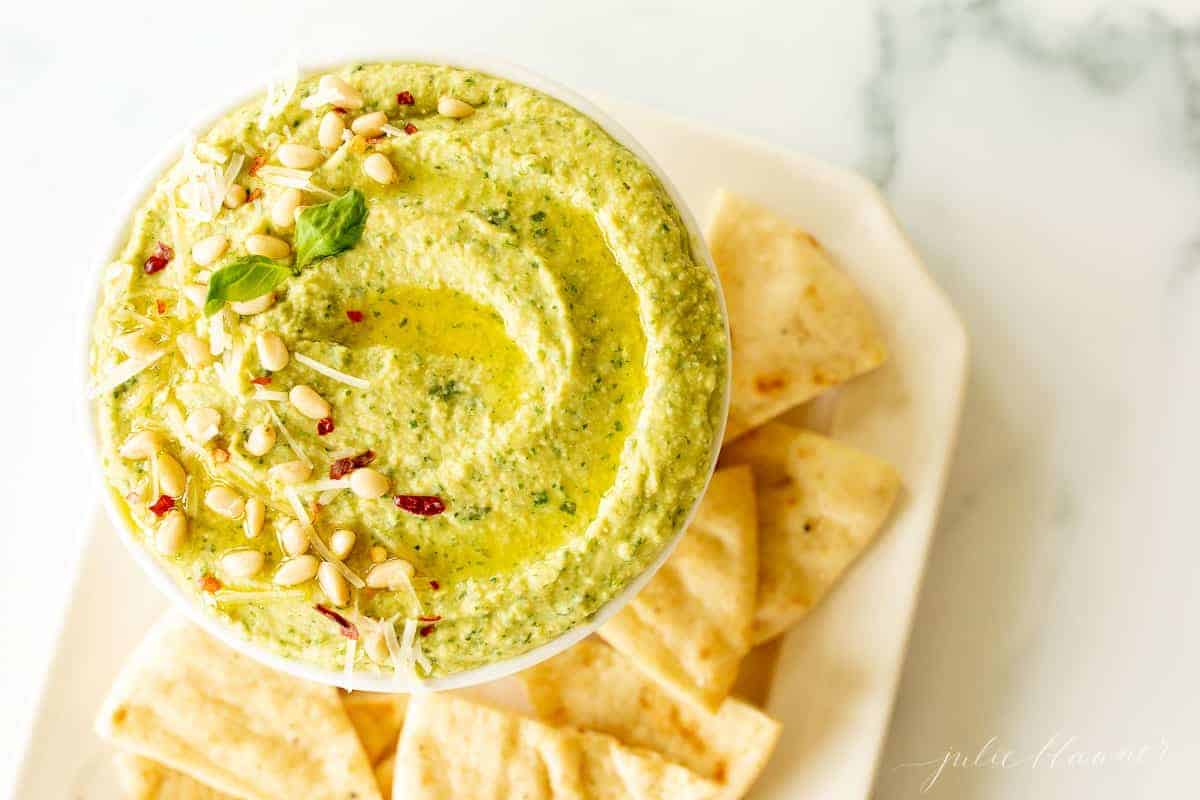 A platter full of pita triangles with a bowl full of pesto hummus.