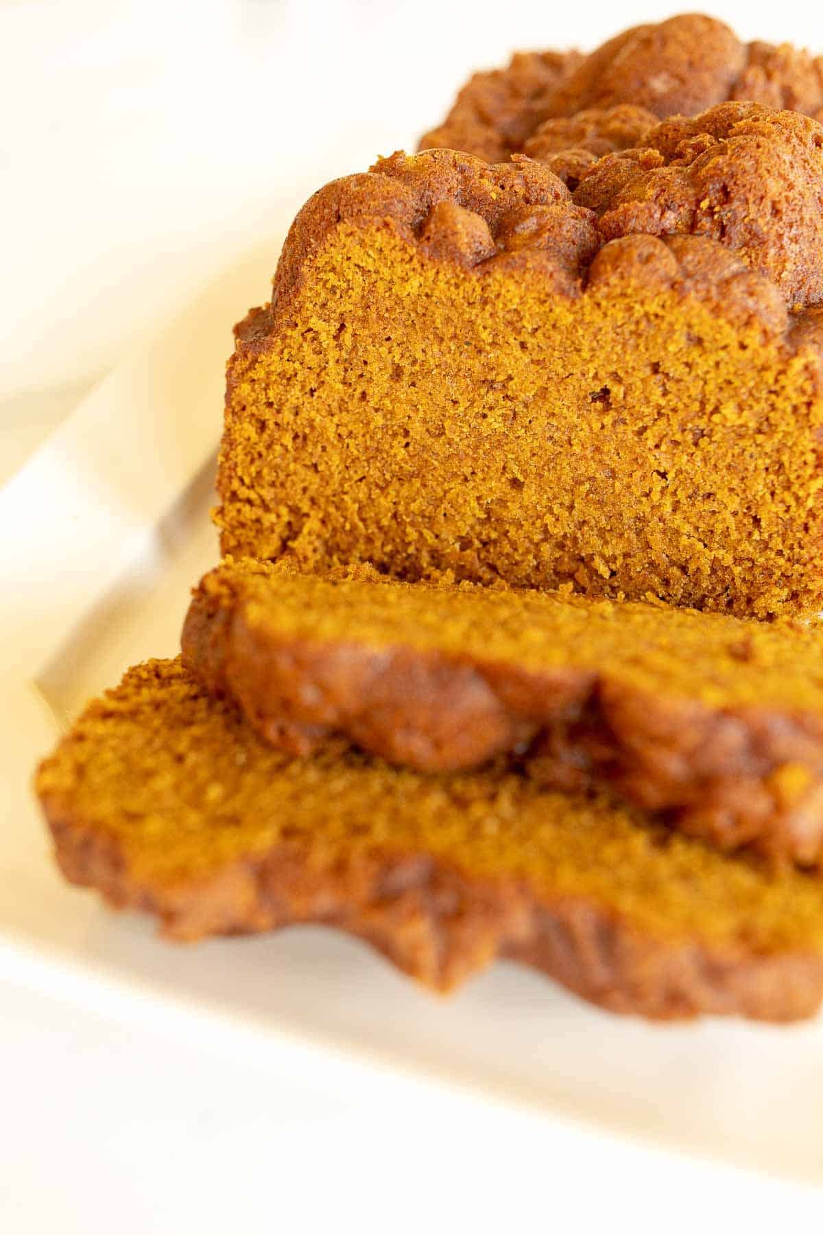 A white platter featuring a loaf of pumpkin bread with slices cut at the front.