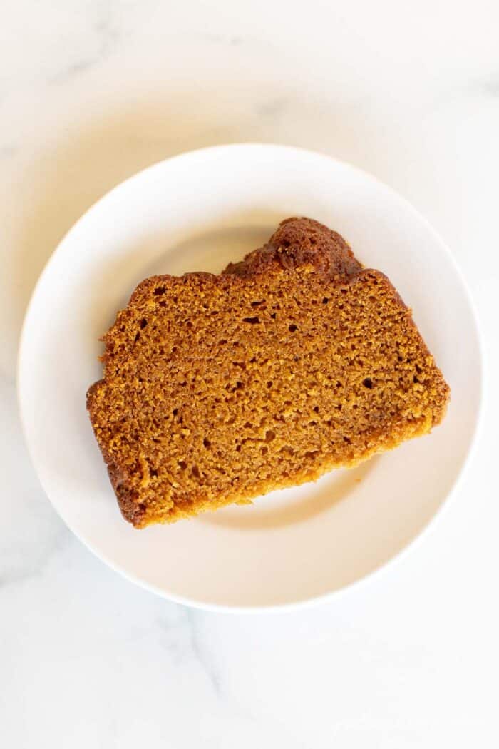 A white plate with a slice of baked pumpkin bread.