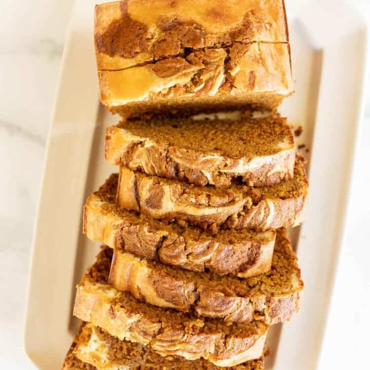A white platter with a loaf of sliced pumpkin cheesecake bread.