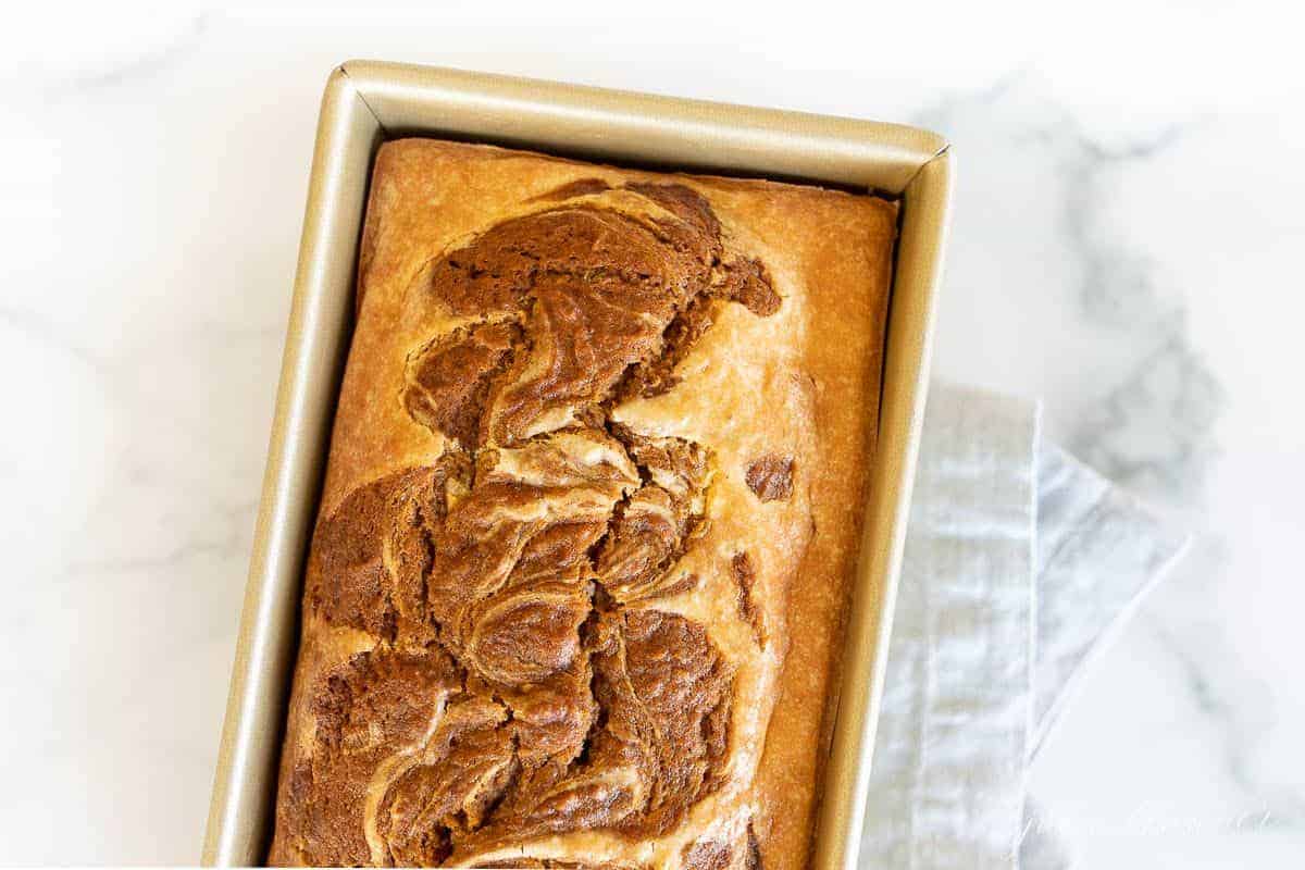 A gold loaf pan filled with baked pumpkin cheesecake bread.