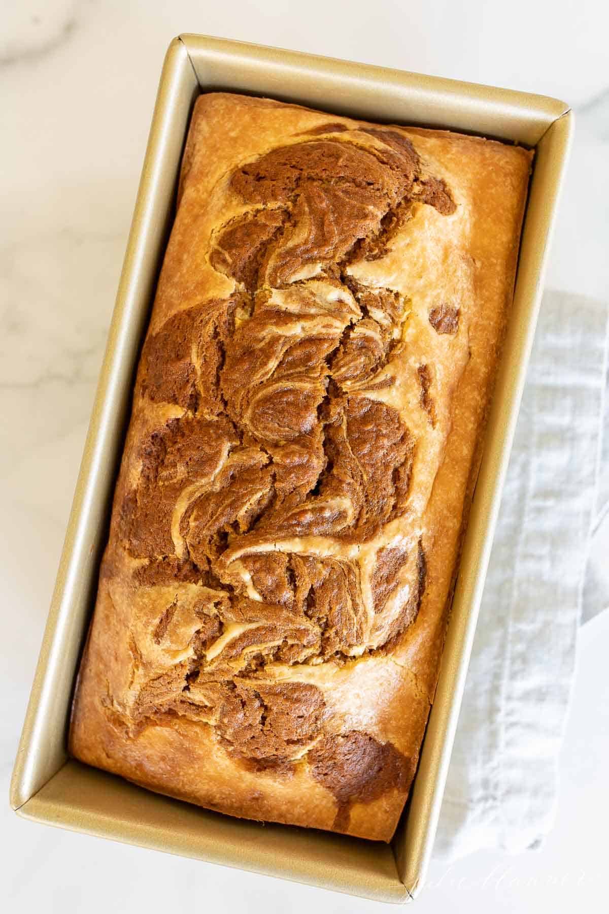 A gold loaf pan filled with baked pumpkin cheesecake bread.