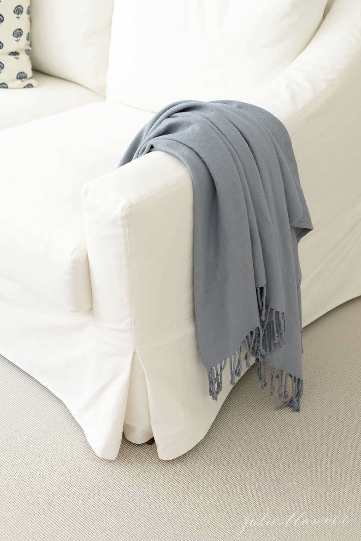 A white sofa draped with a blue blanket on top of a living room rug.