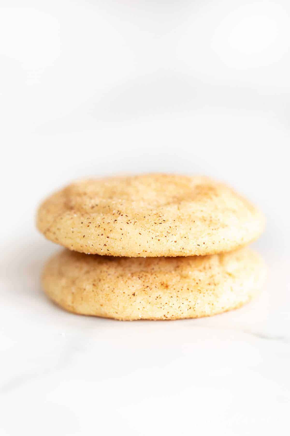 Two Snickerdoodle cookies without cream of tartar stacked on a white surface.