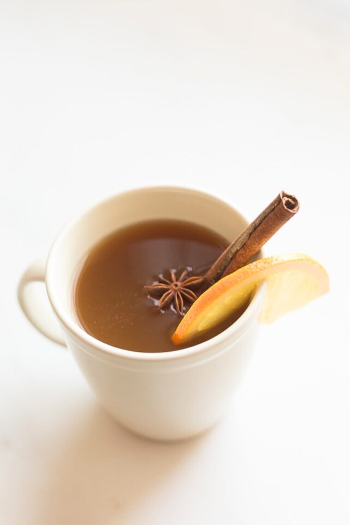 A cup of spiked apple cider garnished with a cinnamon stick, star anise, and a slice of orange.