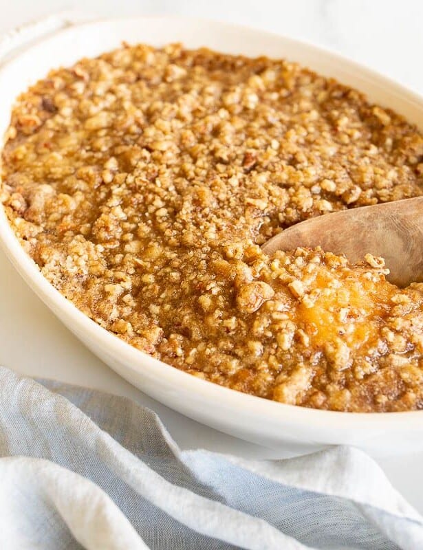 A white oval baking dish filled with a sweet potato casserole, spoon lifting out a serving.