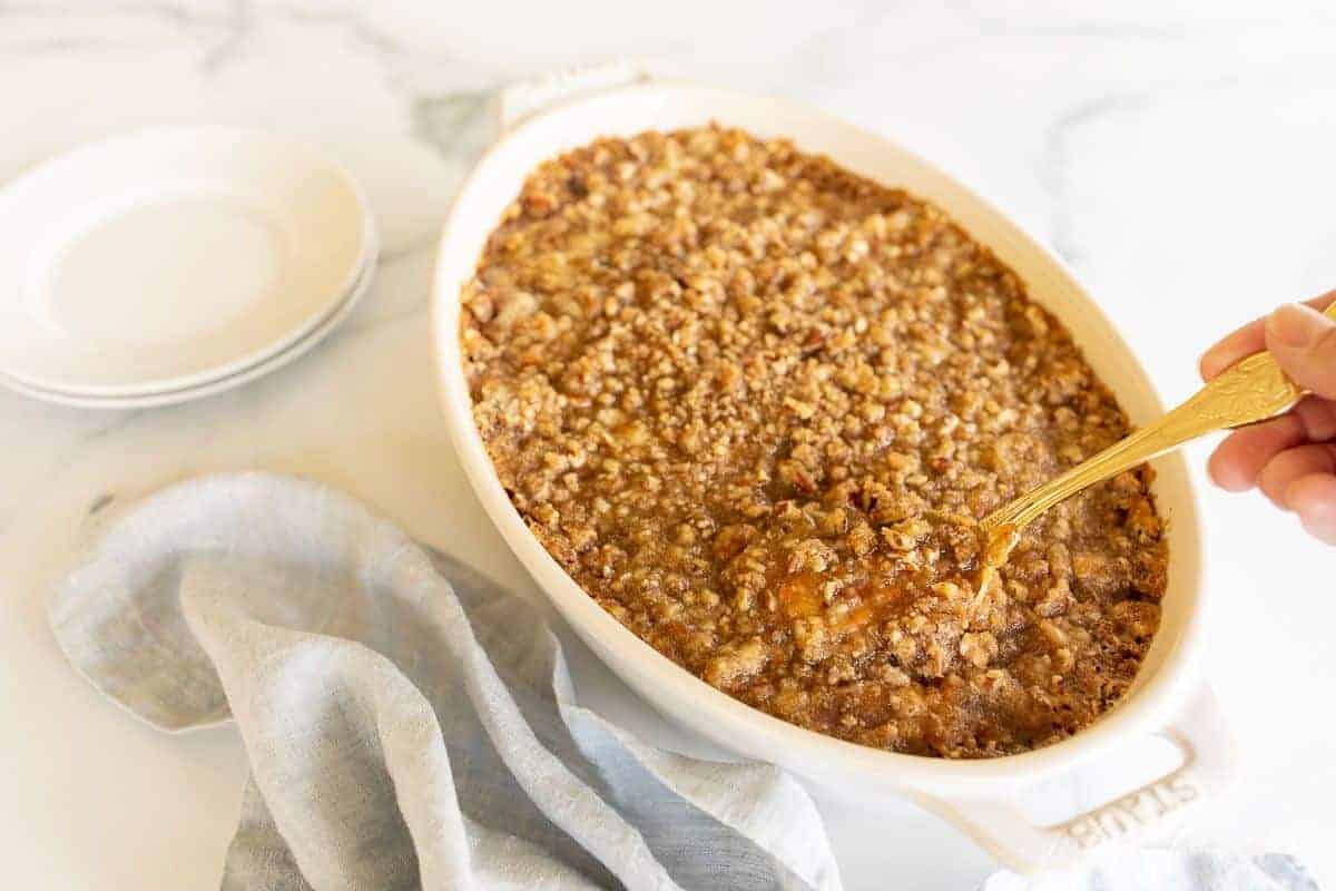 A white oval baking dish filled with a sweet potato casserole, spoon lifting out a serving.