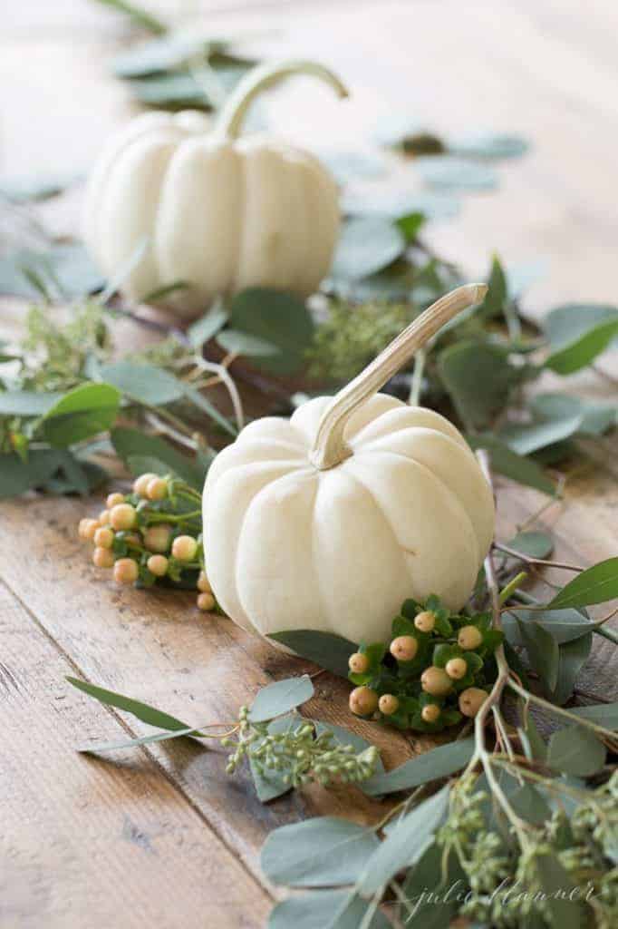 A Thanksgiving centerpiece of pumpkins and greenery on a wood table.