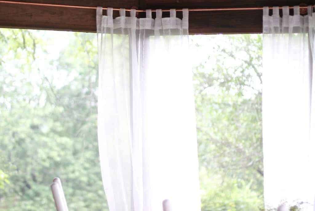 Diy copper curtain rods on a screened porch with white curtain panels.
