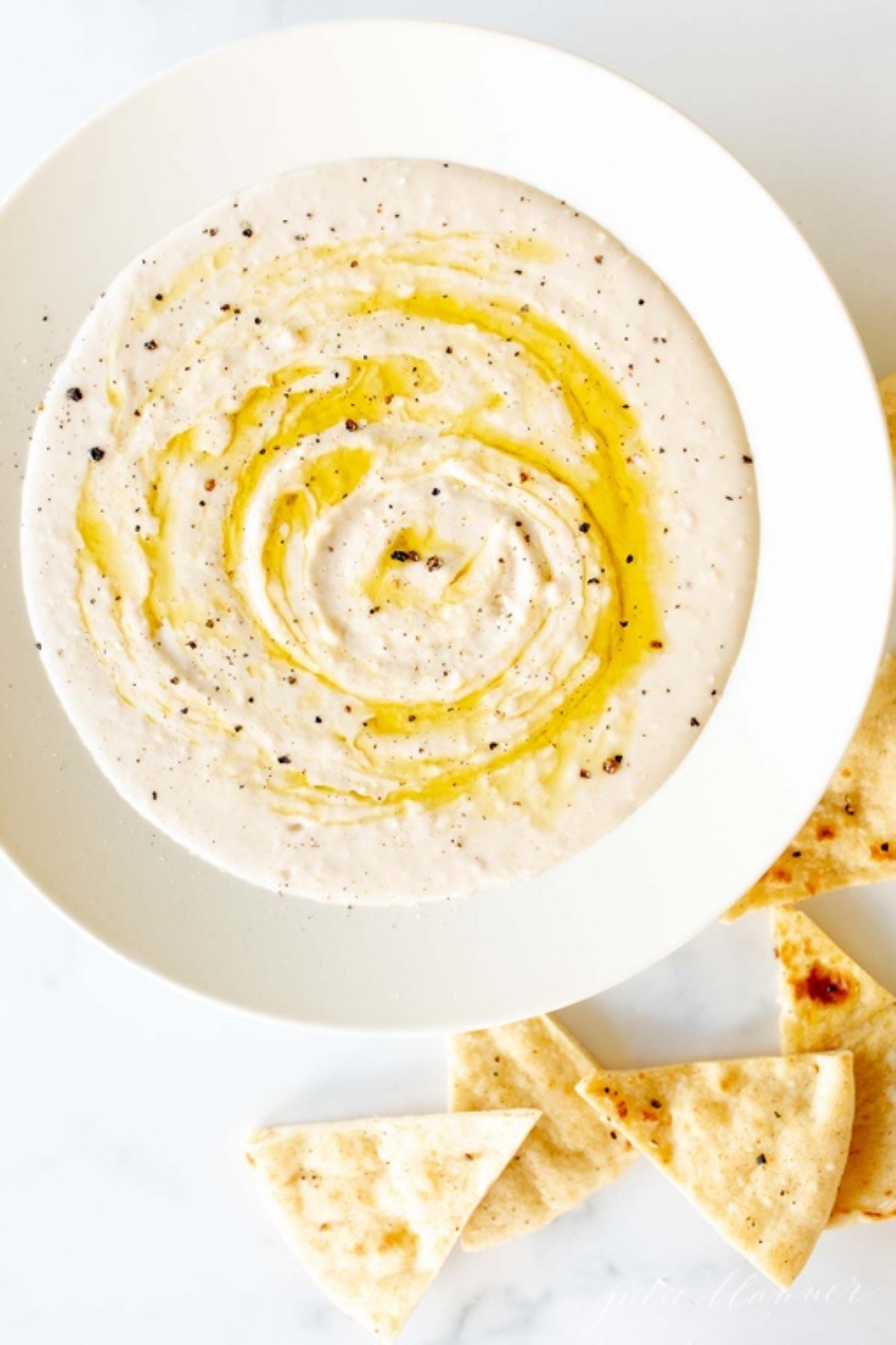 A white bowl of white bean hummus and pita bread to the side.