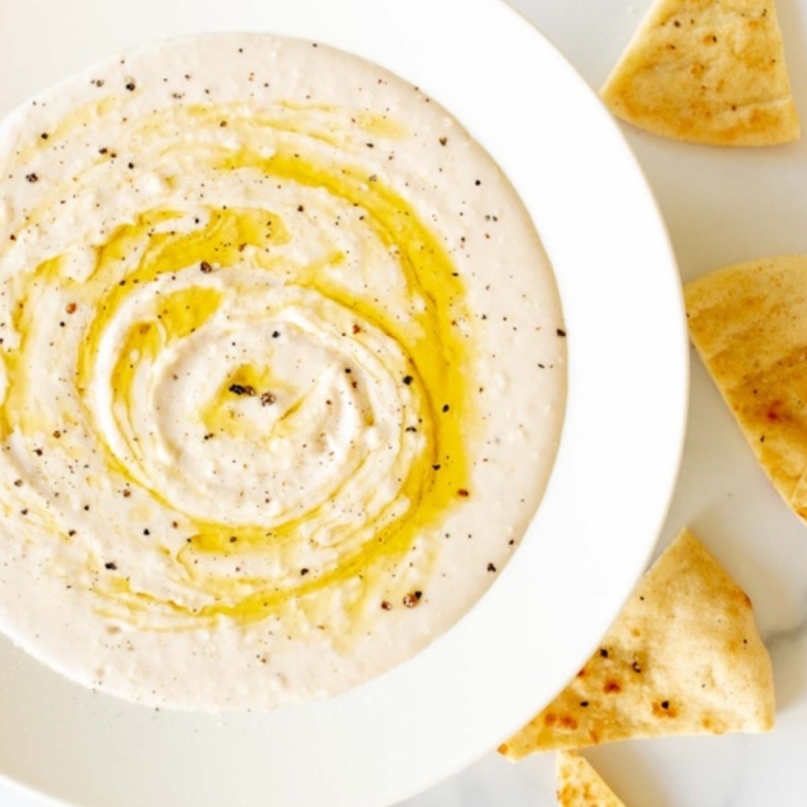 A white bowl of white bean hummus and pita bread to the side.