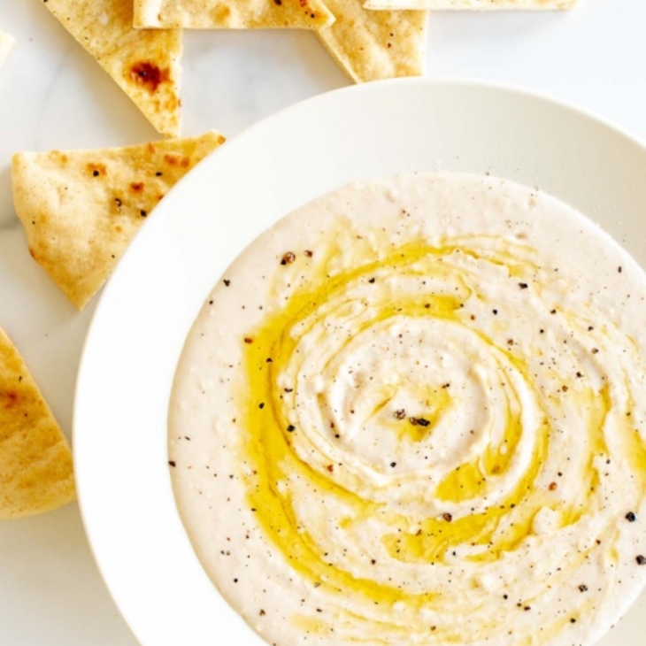 A white bowl of white bean dip and pita bread to the side.