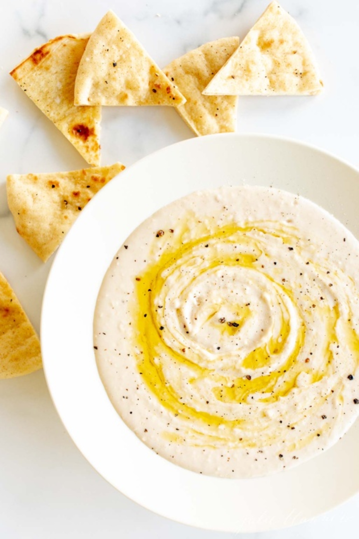 A white bowl of white bean dip and pita bread to the side.