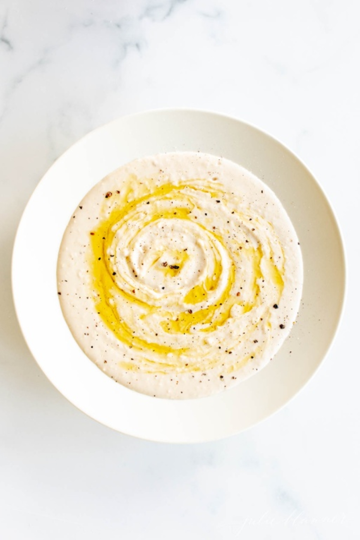 A white bowl full of white bean hummus dip.