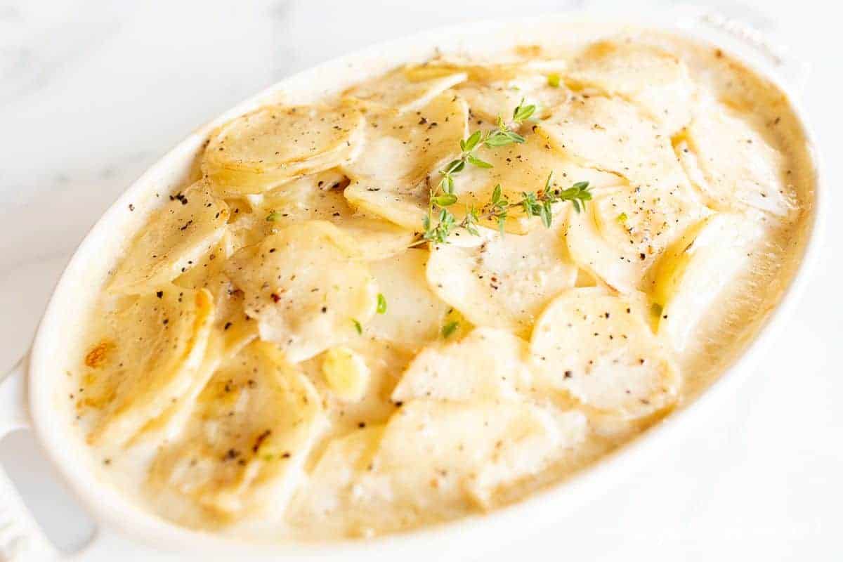 A white oval Staub baker filled with Gratin Dauphinoise potato bake.