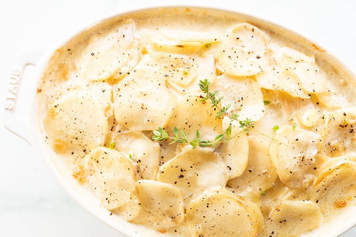 Gratin potatoes in a white oval baking dish, garnished with fresh thyme.